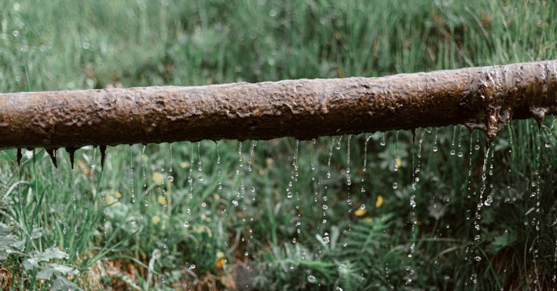 Gutter Cleaning - Rusted metal leaking pipe above grassy meadow